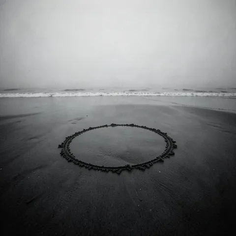 Circle in the Sand cover art: a ring of stones laid on wet sand at the water's edge, in black and white